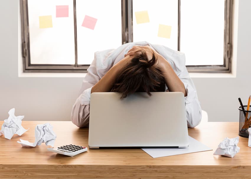 Personne en blouse blanche la tête dans les bras sur un ordinateur, signe de stress intense ou d'épuisement professionnel au travail.