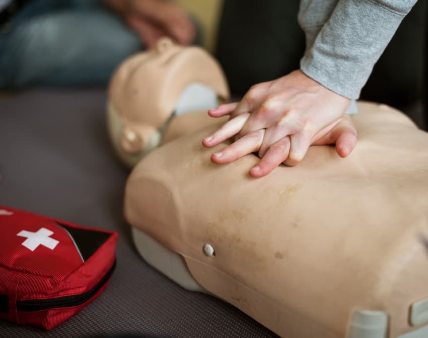 Instructeur de secourisme enseignant la réanimation cardio-pulmonaire (RCP) à un groupe d’adultes. Les participants pratiquent les gestes de premiers secours sur des mannequins, dans une salle lumineuse de formation.