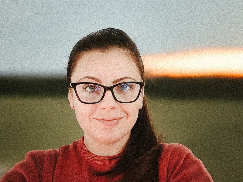 Portrait d'une formatrice souriante portant des lunettes, posant devant un fond clair.