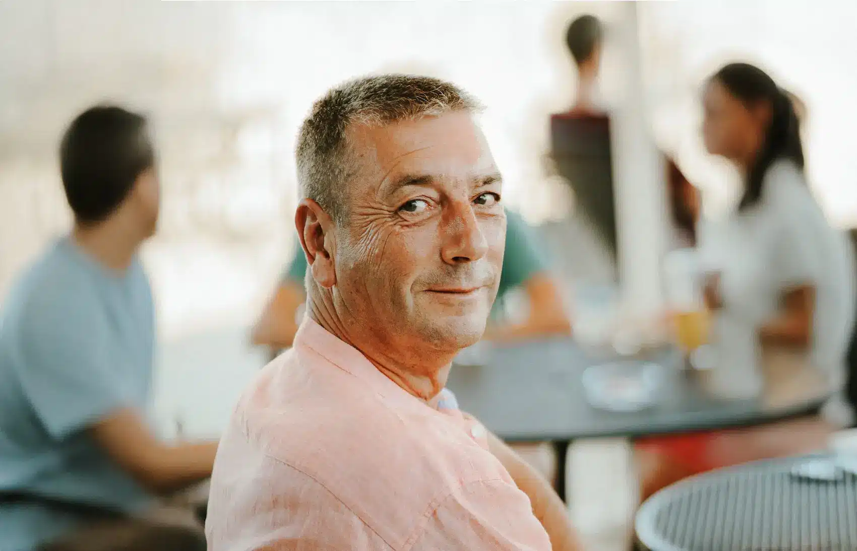 Groupe de collaborateurs en réunion de travail souriante autour d’une table, échangeant des idées et travaillant ensemble dans un environnement lumineux.