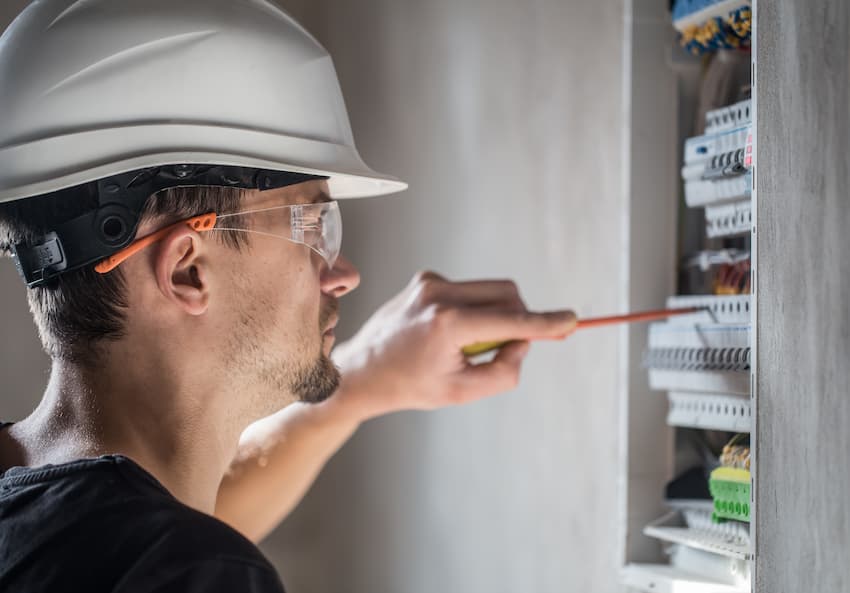 Technicien équipé d'un casque et de lunettes de protection intervenant sur un tableau électrique, illustrant les niveaux d'habilitation électrique H0B0, B0 et BS.