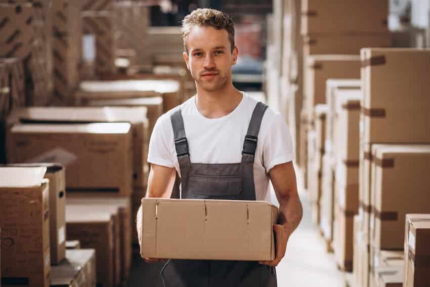 Agent logistique portant un carton dans un entrepôt, illustrant les gestes de manutention enseignés en formation PRAP IBC.