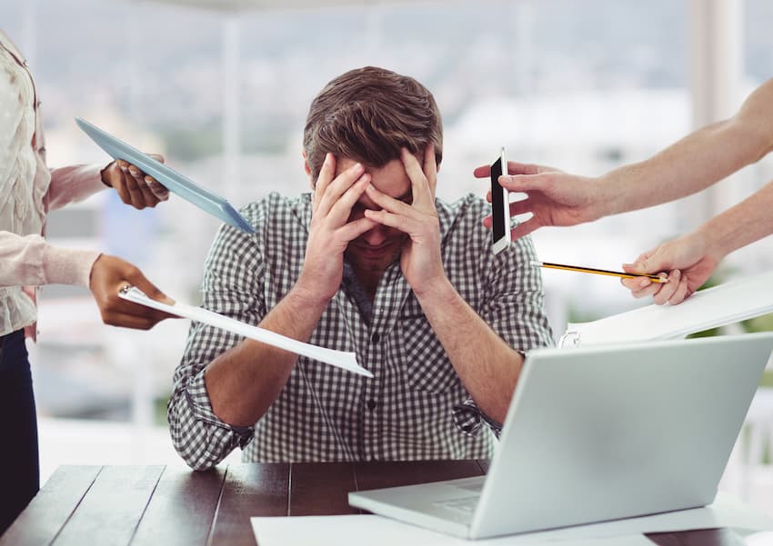 Salarié en situation de surcharge de travail se tenant la tête entre les mains, illustrant les signes d'épuisement professionnel et de burn-out au travail.