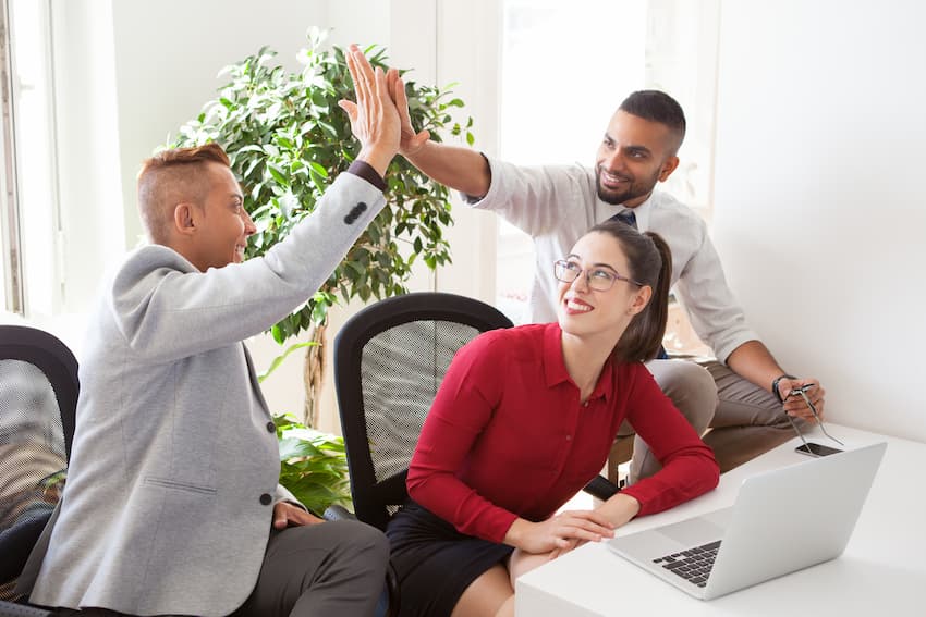Équipe de salariés épanouis se faisant un high five au bureau, illustrant les bénéfices d'une démarche QVCT réussie sur le bien-être et la cohésion en entreprise.
