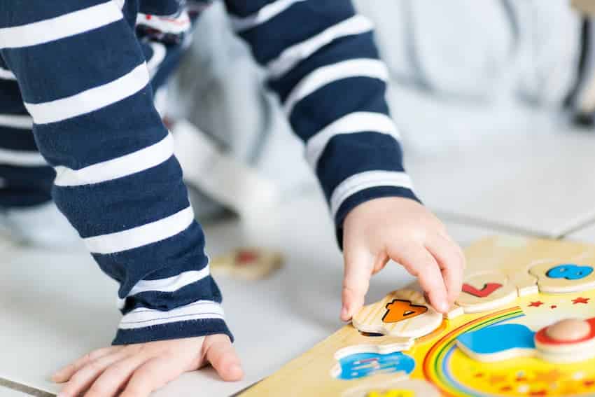 Jeune enfant jouant au sol avec un puzzle en bois dans une structure d'accueil, illustrant les activités au sol à l'origine des risques physiques en formation PRAP Petite Enfance.