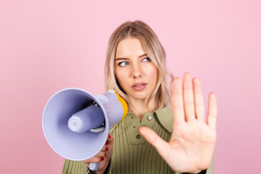 Femme tenant un mégaphone et faisant un geste d'arrêt, illustrant le rôle du référent harcèlement CSE dans la prévention du harcèlement sexuel en entreprise.