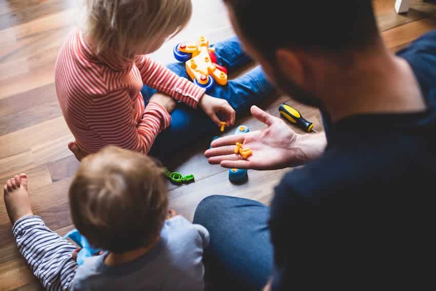 Professionnel de la petite enfance assis au sol avec deux enfants lors d'une activité de jeu, illustrant les postures au sol enseignées en formation PRAP Petite Enfance.