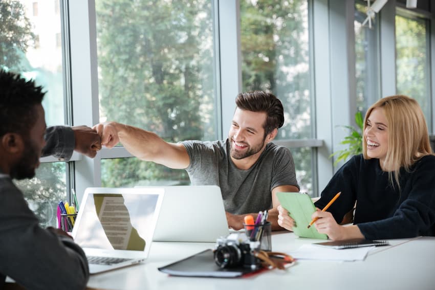 Collègues souriants travaillant ensemble dans un open space, illustrant l'amélioration de la qualité de vie et des conditions de travail dans le cadre d'une démarche QVCT en entreprise.