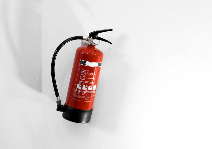 Extincteur rouge fixé à un mur blanc avec son pictogramme de classes de feu, illustrant les moyens d'extinction à maintenir opérationnels et le recyclage de la formation EPI.