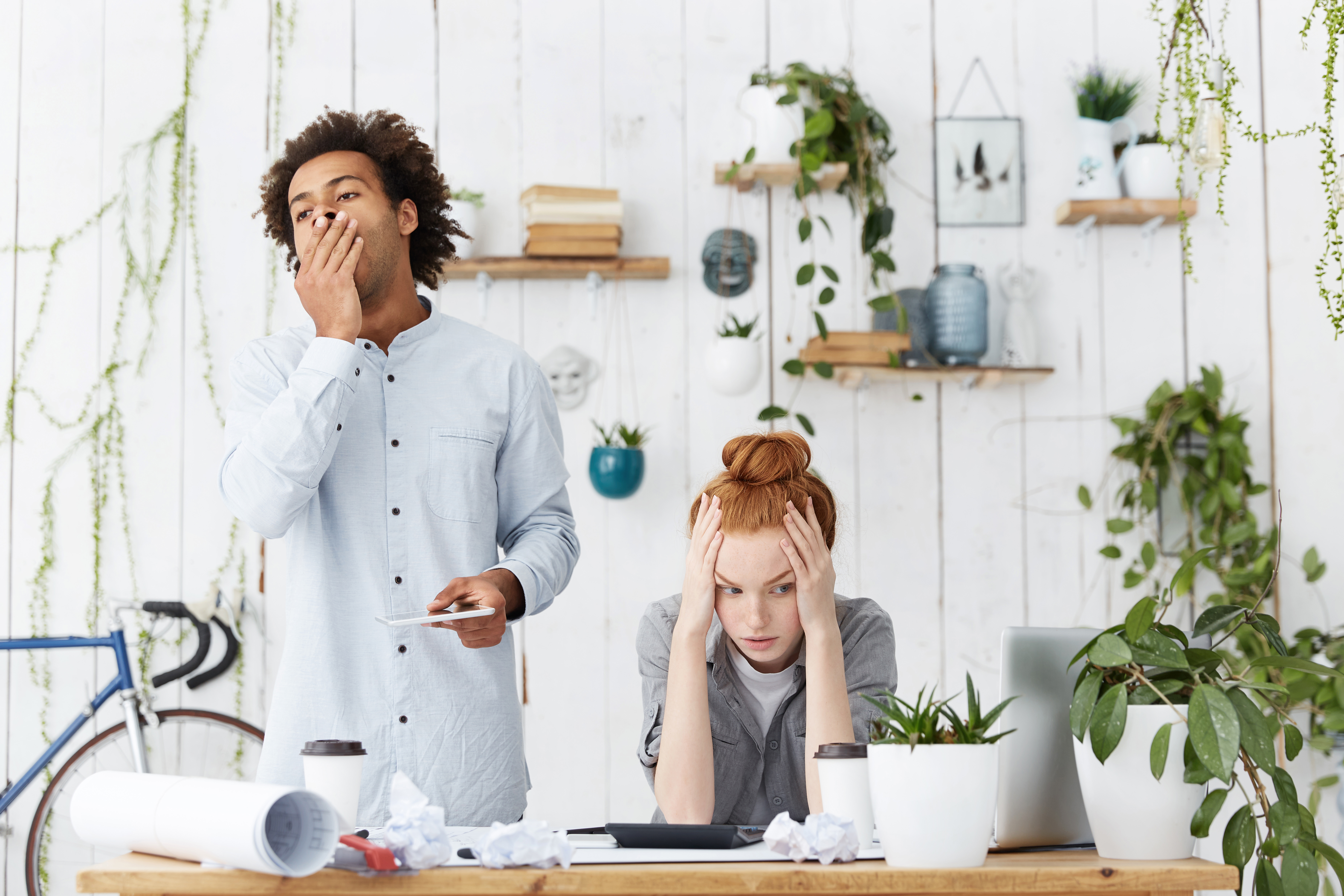 Jeune professionnelle submergée par la fatigue et la sursollicitation cognitive à son poste de travail, entourée de papiers froissés et de gobelets de café.