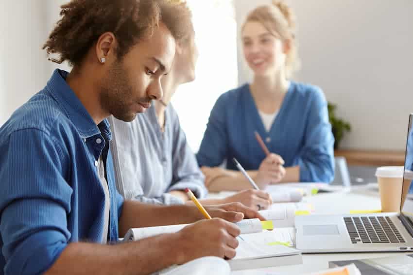 Salariés en session de formation prenant des notes avec un ordinateur portable, illustrant le choix entre une formation gestes et postures et une formation PRAP en entreprise.