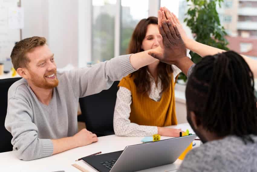 Collègues se donnant un high five lors d'une réunion, illustrant des relations professionnelles apaisées grâce à une communication assertive au travail.