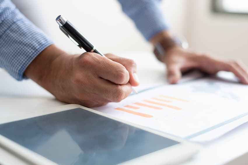 Responsable annotant un tableau de données avec un stylo, illustrant le suivi des échéances de certification des salariés en entreprise.
