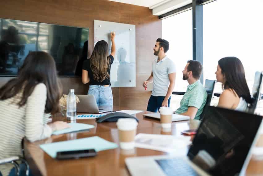 Salariés réunis en salle autour d'une présentation au tableau, illustrant le recensement des formations obligatoires en entreprise.