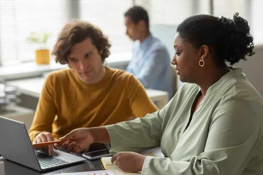 Deux collègues examinant un document sur un ordinateur portable dans un bureau.