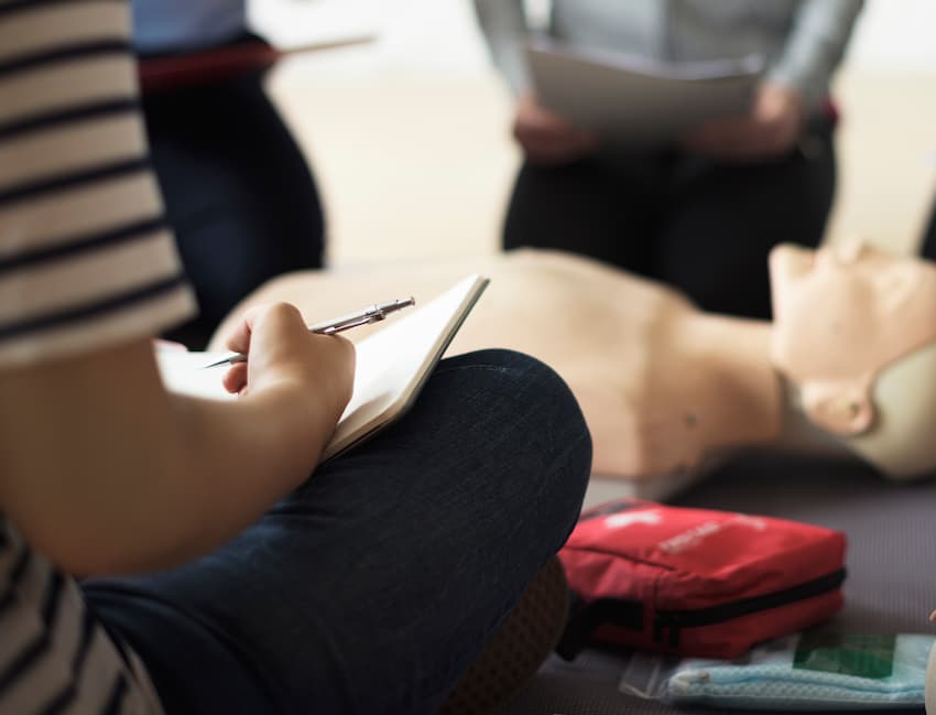 Stagiaires prenant des notes autour d'un mannequin de réanimation lors d'une formation aux gestes de secours.