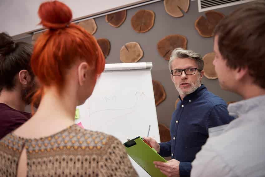 Formateur animant une séquence devant un paperboard face à un petit groupe de stagiaires.