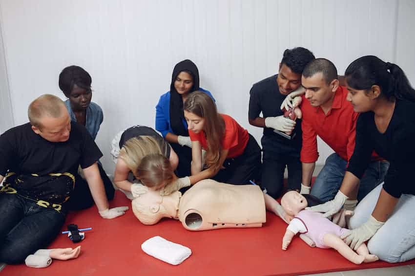 Groupe de collaborateurs s'entraînant aux gestes de premiers secours sur mannequins adulte et nourrisson lors d'une session de formation en entreprise.