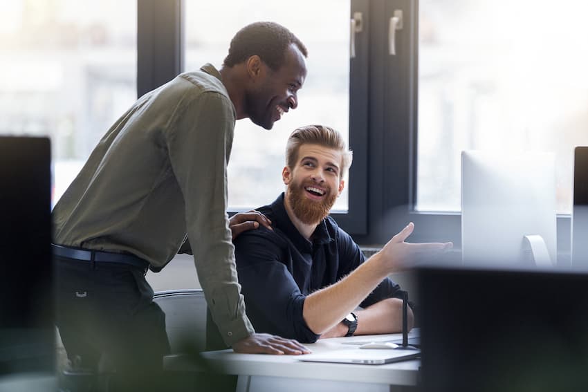 Un manager échange avec un collaborateur assis à son poste de travail, dans un bureau ouvert.